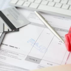 Image of a calculator, credit cards, pen and piggy bank sitting atop an invoice marked 