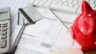 Image of a calculator, credit cards, pen and piggy bank sitting atop an invoice marked "Paid."