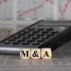 Image of three dice spelling out M&A sitting in front of a calculator, with business graphs in the background