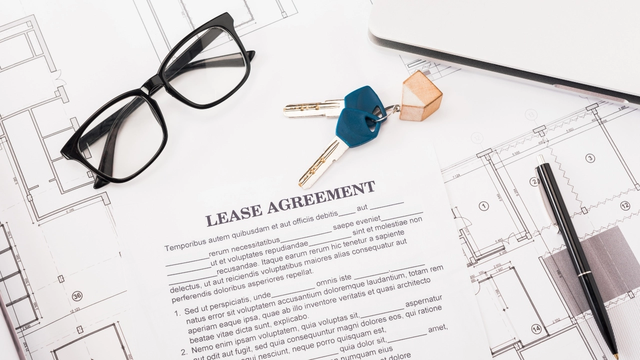 Image of a pair of eyeglasses, keys, pen and latptop sitting atop a lease agreement