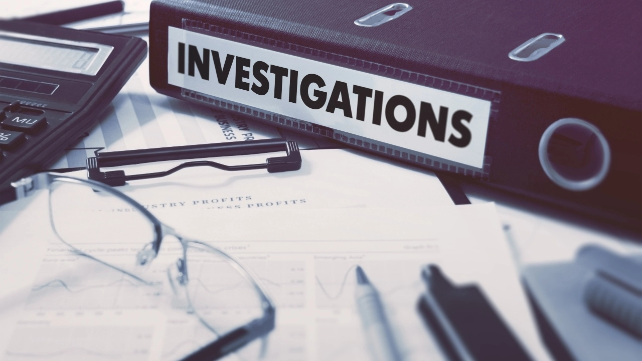 Image of a binder with "Investigations" inscription sitting on a desk with eyeglasses, a calculator, documents and writing utensils