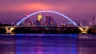 Image of the Lowry Avenue Bridge, lighted blue at dusk, with Minneapolis skyline in the background