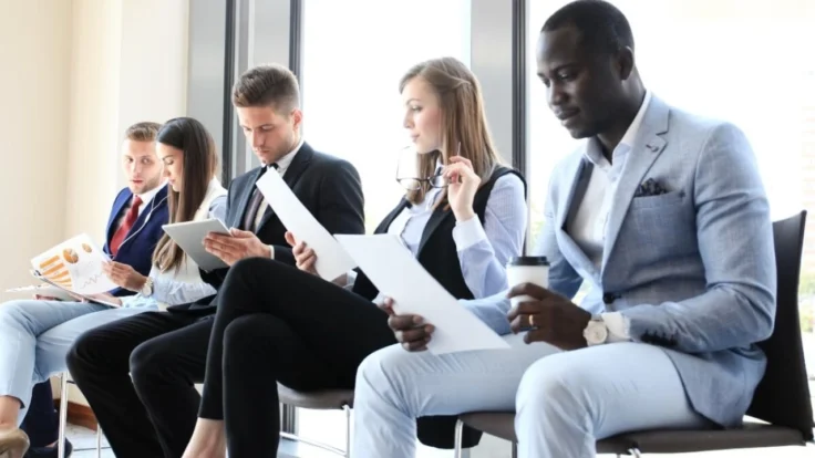 Image of five seated job applicants awaiting interviews
