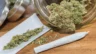 Image of a pre-roll and ground flower sitting atop a rolling paper in front of a jar of flower