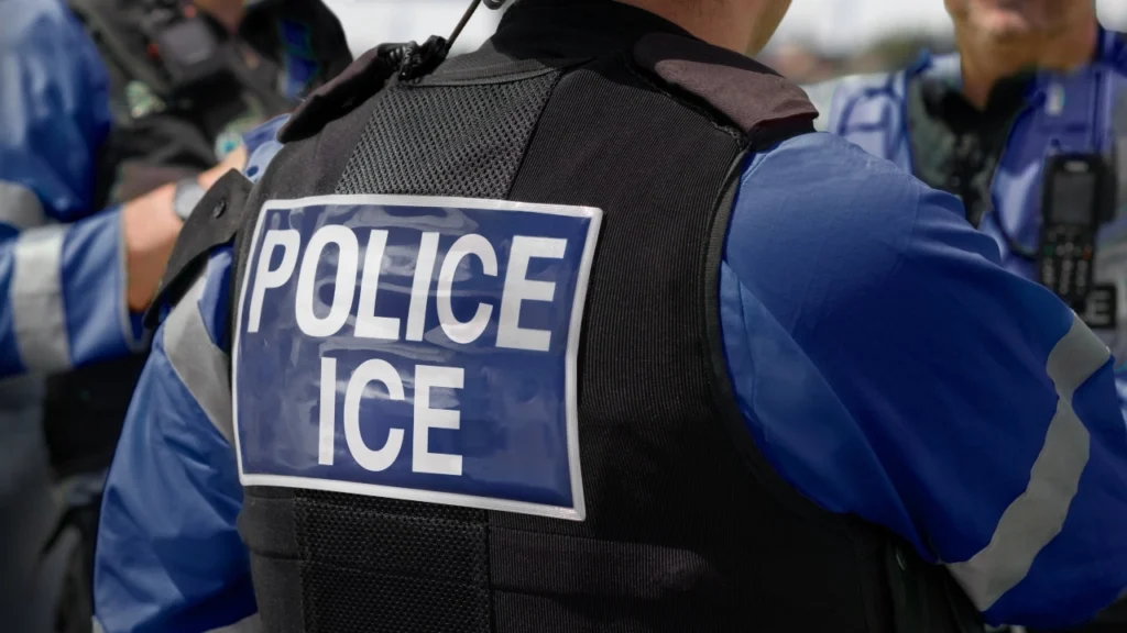 Image of the back of an ICE officer standing with fellow officers at the scene of an incident
