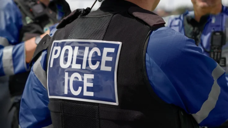 Image of the back of an ICE officer standing with fellow officers at the scene of an incident